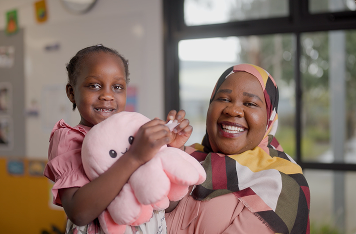 A woman hugging her daughter, both smiling at the camera