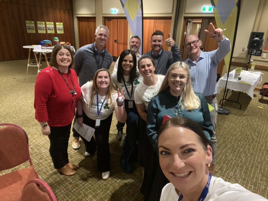 A group of people pose for a cheerful selfie in a conference room
