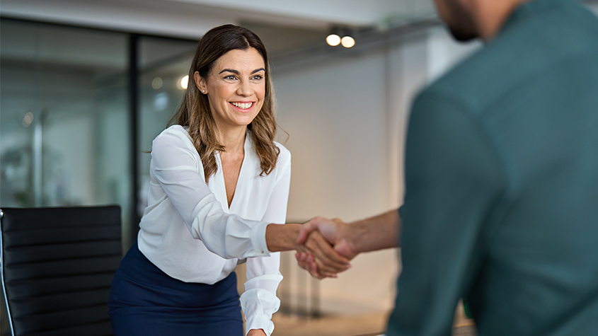 Woman leaning over desk to shake man's hand