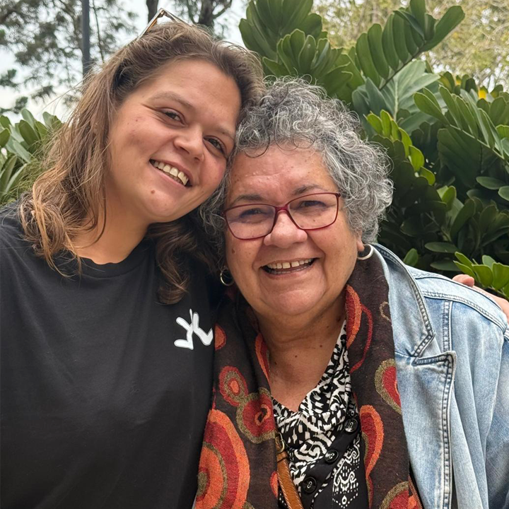 Two people standing side by side, one with their arm around the other, both are facing the camera.