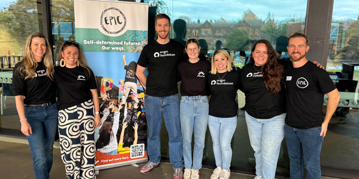 Seven people in black branded T-shirts stand together beside an EPIC banner promoting self-determined futures at a partnership event.