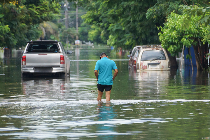 Man in blue shirt walking down the middle of a flooded residential street
